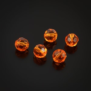 May include: Five orange crystal beads on a black background