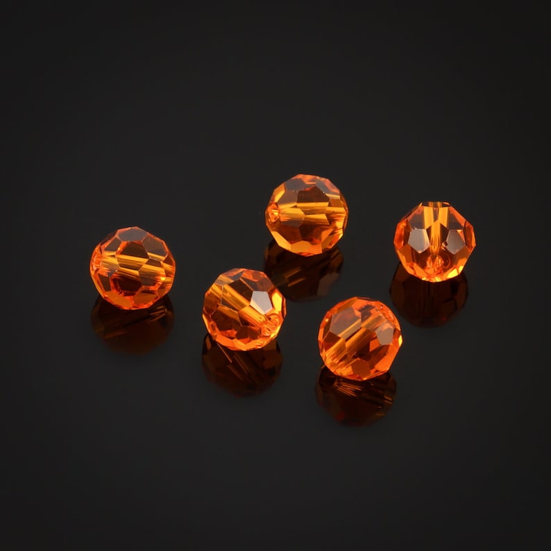 May include: Five orange crystal beads on a black background
