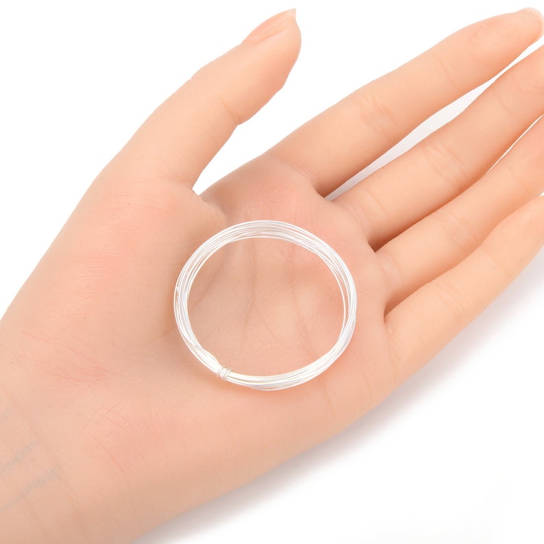 May include: A coil of silver wire, approximately 20 gauge, is shown in a hand. The wire is coiled into a circle and is ready for jewelry making.
