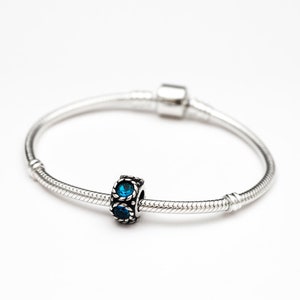 May include: A silver charm bracelet with a blue crystal charm. The charm has a silver frame with a decorative design.