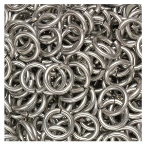 May include: A close-up view of a pile of silver metal rings. The rings are all the same size and shape, and they are arranged in a random pattern.