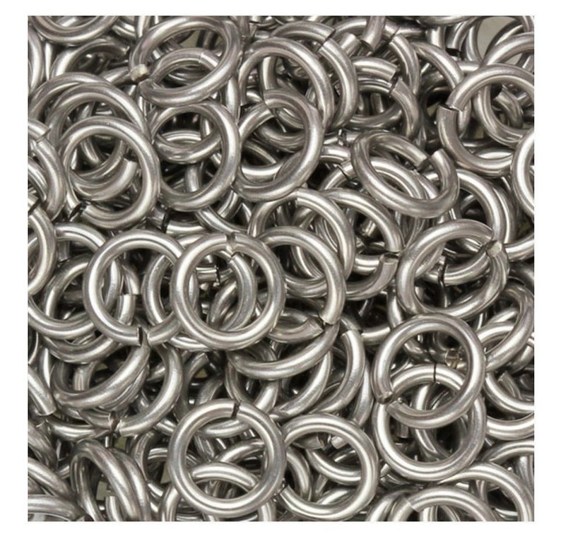 May include: A close-up view of a pile of silver metal rings. The rings are all the same size and shape, and they are arranged in a random pattern.