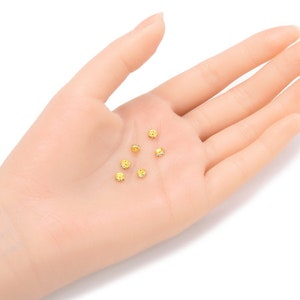 May include: A close-up of a hand holding six small, round, gold-colored beads with yellow rhinestones. The beads are for jewelry making.