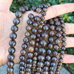 May include: A collection of brown wood beads with a dark brown and gold marbled pattern. The beads are strung on a clear string and are arranged in a fan shape.