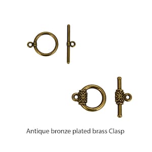 Może przedstawiać: Dwa antyczne, brązowe, pozłacane zapięcia. Jedno zapięcie to prosty okrągły pierścień z prętem, drugie ma ozdobny wzór kwiatowy.