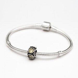 May include: A silver charm bracelet with a single charm featuring three yellow gemstones.