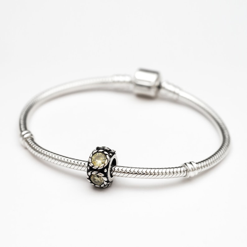 May include: A silver charm bracelet with a single charm featuring three yellow gemstones.