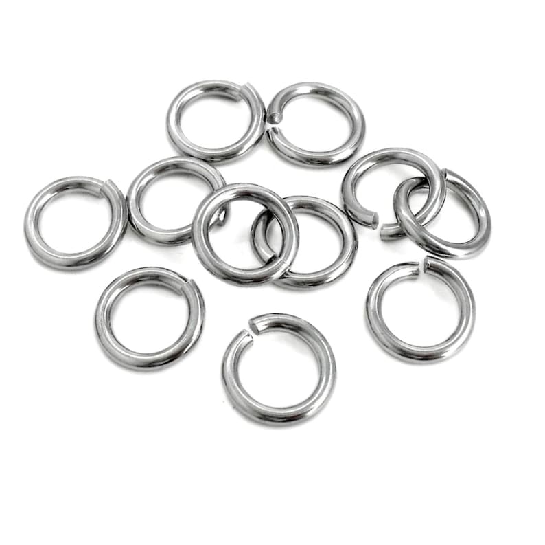 May include: A group of silver jump rings, a type of jewelry finding, scattered on a white background.