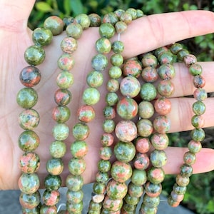 May include: A strand of green, red, and brown gemstone beads. The beads are round and have a speckled pattern.