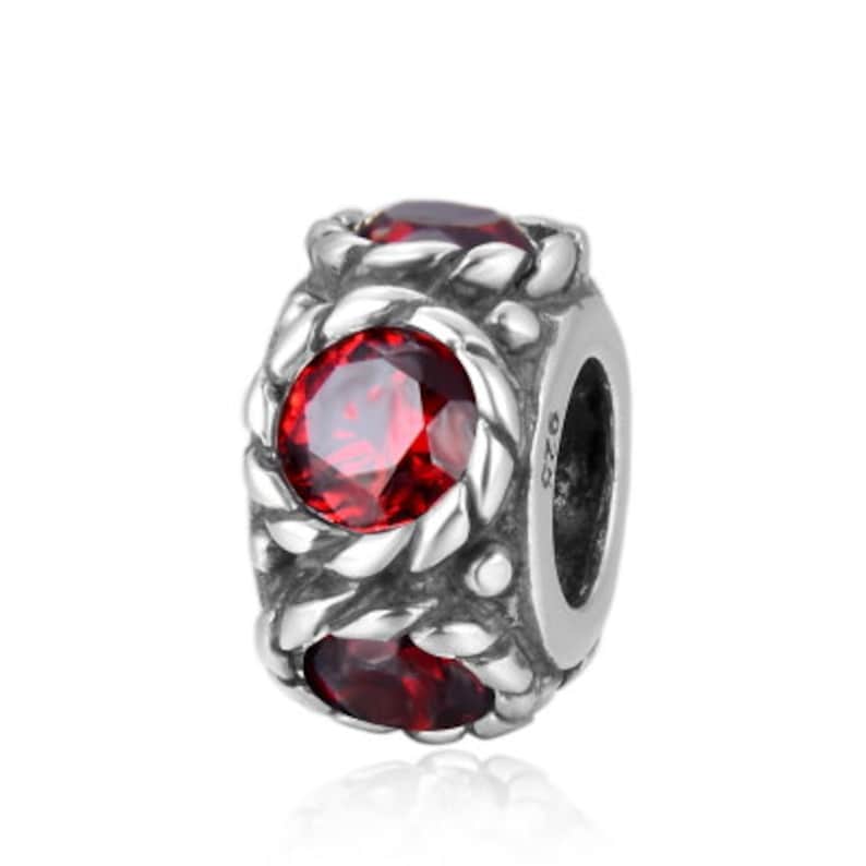May include: Silver charm featuring three red gemstones set in a braided design. The charm has a silver clasp and the number "925" stamped on the side.