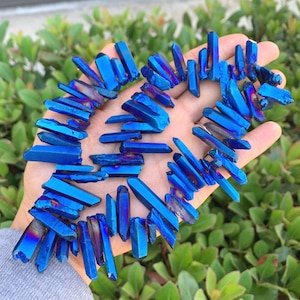 Puede incluir: Una hebra de puntas de cristal de cuarzo titanio azul, también conocido como cuarzo fantasma azul, dispuestas en forma de corazón. Los cristales son iridiscentes y tienen un brillo metálico.