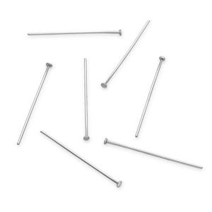 May include: A set of eight silver head pins scattered on a white background. The pins are straight and have a small round head at one end.