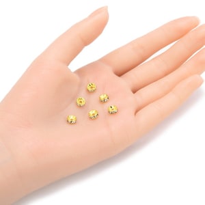 May include: Six gold-toned metal bead caps with clear rhinestones. The bead caps are round and have a flat back.