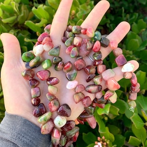 May include: A strand of green, pink, and red tumbled gemstone beads. The beads are irregular in shape and have a natural, polished finish.