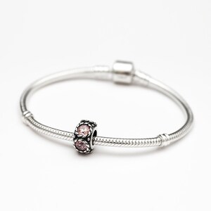 May include: A silver charm bracelet with a single charm featuring two pink gemstones set in a silver frame.