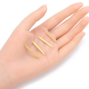 Könnte beinhalten: Fünf goldfarbene Metall-Stangenverbinder mit jeweils zwei Löchern. Die Verbinder sind versetzt auf einer Hand angeordnet.