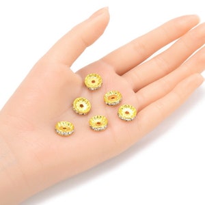 May include: A close-up of seven gold-toned metal bead caps with clear rhinestone accents. The bead caps are arranged on a hand.