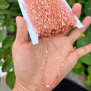 May include: Rose gold-colored chain in a roll, with a section of the chain extended. The chain is made of small, rectangular links. The word "adabele" is visible on the packaging. This chain is suitable for jewelry making.