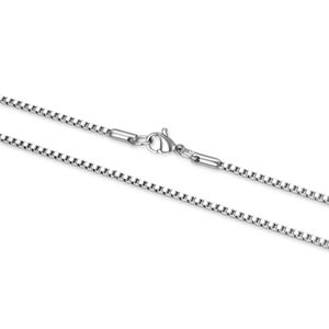 May include: A silver chain necklace with a lobster clasp closure. The chain is made of small, square links.