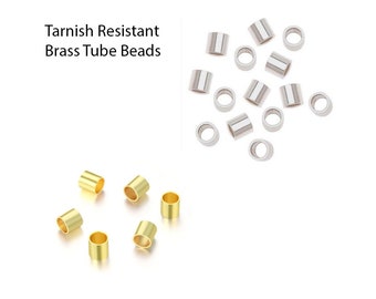 May include: An assortment of brass and silver-coloured tube beads are shown against a white backdrop. The text "Tarnish Resistant Brass Tube Beads" is in the upper left. The beads are cylindrical with a central hole.