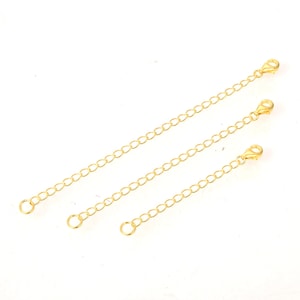 May include: Three gold chain extenders of different lengths. Each extender has a lobster clasp on one end and a jump ring on the other.