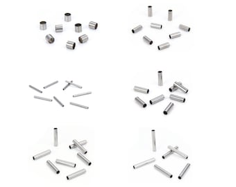 May include: A collection of small, cylindrical metal tubes. The tubes are silver in color and appear to be made of stainless steel. The tubes are of varying lengths and diameters, and are arranged in several groups against a white background.
