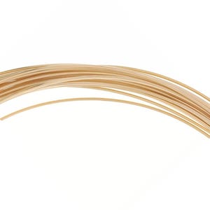 Puede incluir: Primer plano de un haz de alambre fino de color dorado, probablemente para la fabricación de joyas o manualidades. El alambre está dispuesto en un patrón curvo y fluido sobre un fondo blanco. El alambre parece liso y brillante.