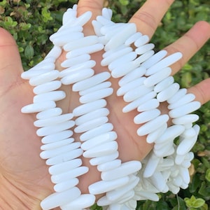 Peut inclure: Un brin de perles blanches, lisses et ovales. Les perles sont disposées en quinconce, créant une texture visuellement attrayante.