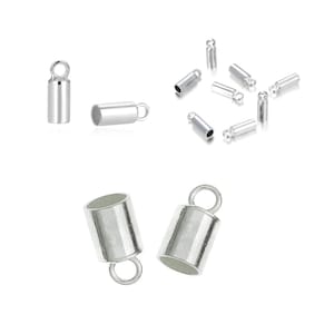 Puede incluir: Tapones de extremo de metal plateados para la elaboración de joyas. Los tapones de extremo tienen una forma cilíndrica con un pequeño bucle en la parte superior. Algunos tapones de extremo se muestran individualmente, mientras que otros están dispersos sobre un fondo blanco.