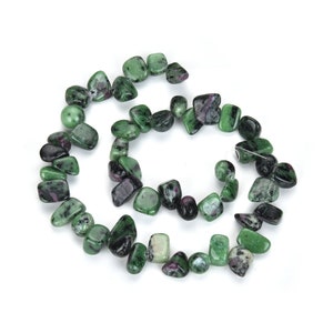 May include: A strand of tumbled zoisite beads with ruby inclusions. The beads are a mix of green and dark green, with flecks of red ruby. The beads are strung together on a thin, clear string, perfect for jewelry making.