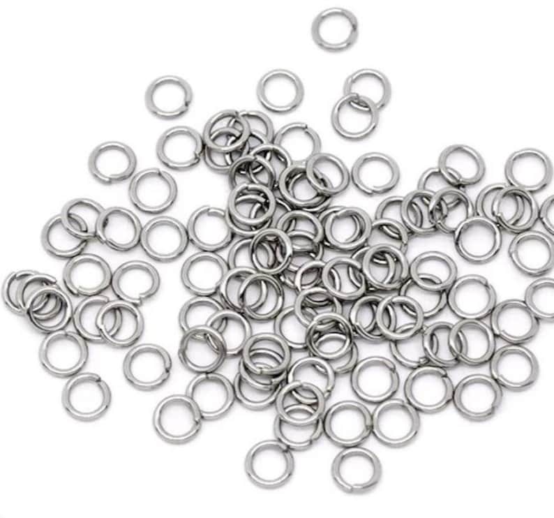 May include: A large pile of silver jump rings, a type of jewelry finding used for connecting chains, cords, and other jewelry components.