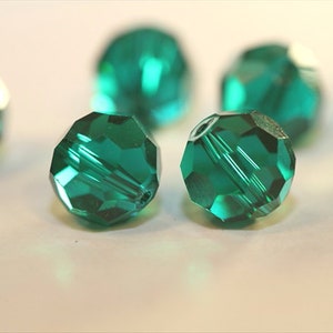 May include: Close up of emerald green faceted glass beads. The beads are round and have a shiny, reflective surface.