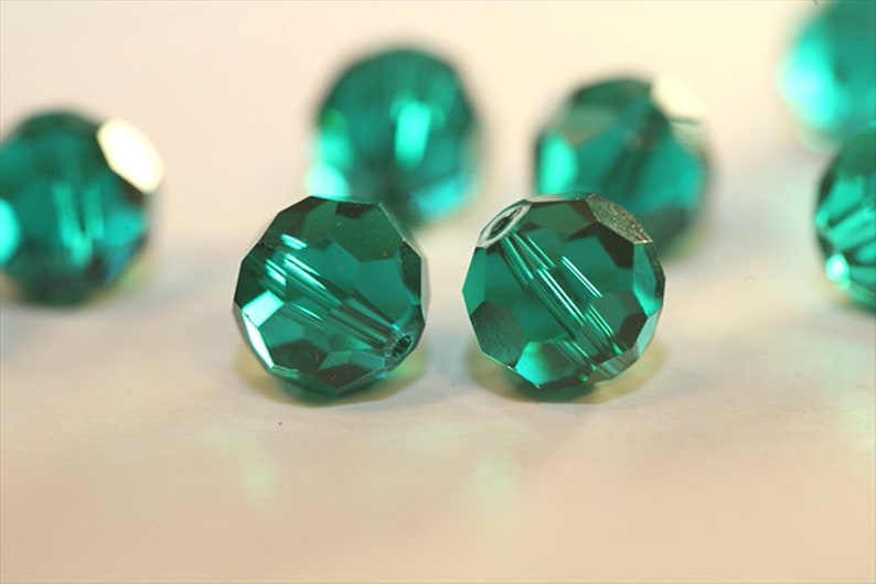 May include: Close up of emerald green faceted glass beads. The beads are round and have a shiny, reflective surface.