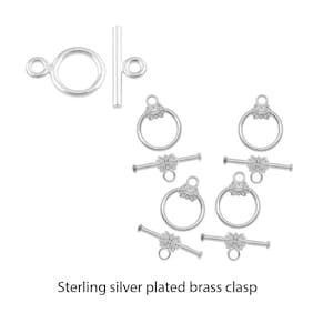 May include: Sterling silver plated brass clasp with a decorative floral design. The clasp is made up of two parts: a round ring with a floral design and a bar with a loop on each end.