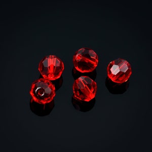 May include: Five red crystal beads on a black background