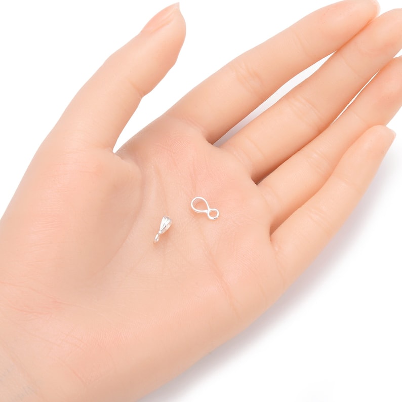 May include: Two silver-toned jewelry findings, a small teardrop-shaped pendant bail and a small figure-eight jump ring, on a white surface.