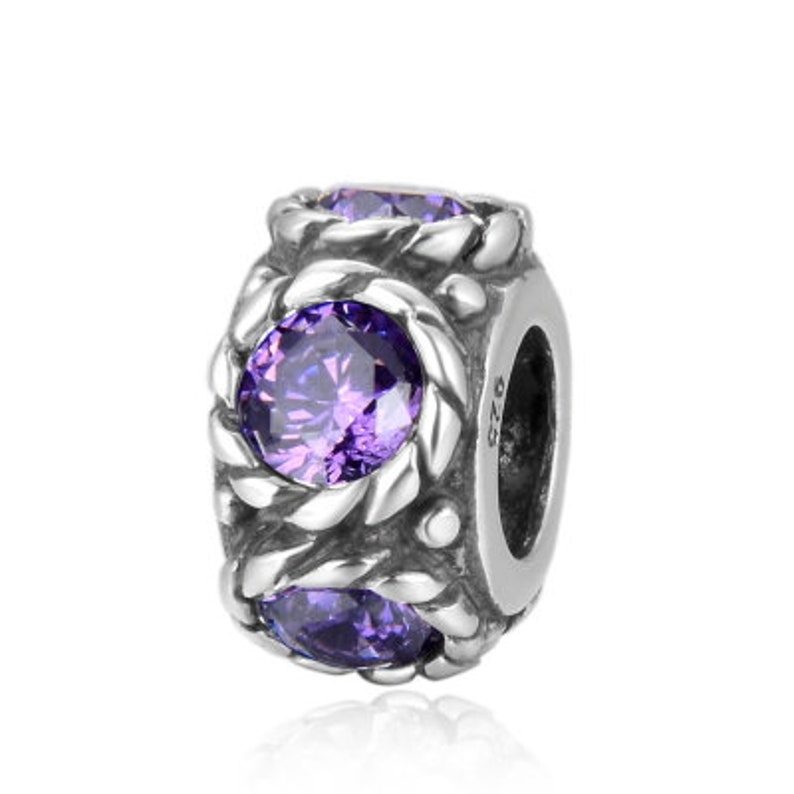 May include: Silver charm with a braided design and three purple gemstones. The charm has a hole for attaching to a bracelet.