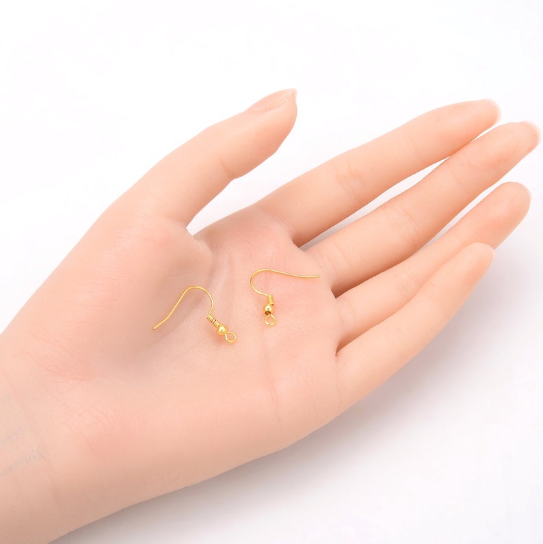 May include: Two gold earring hooks with a small ball at the top of the hook.