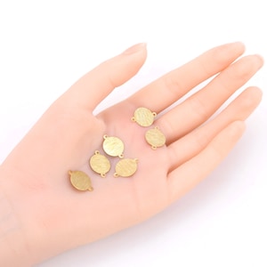 May include: A set of eight gold-toned metal circle charms with two jump rings on each charm. The charms are on a hand.