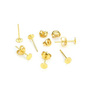 May include: A collection of gold-colored earring posts and backs, displayed against a white background. The posts have a flat, round base for attaching earrings. The backs include butterfly and other styles.