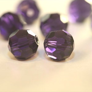 May include: A group of purple crystal beads with a faceted design. The beads are round and have a shiny finish.