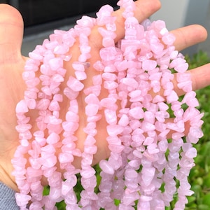 Könnte beinhalten: Eine Strähne rosafarbener Rosenquarz-Chipsteine. Die Steine sind unregelmäßig geformt und haben eine natürliche, getrommelte Oberfläche.