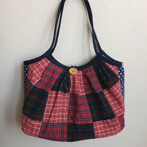 Puede incluir: Un bolso tote patchwork con un diseño de cuadros rojos, azul marino y blancos. El bolso presenta un cierre de botón de madera y asas azul marino. Los lados del bolso son blancos con lunares azul marino. Un accesorio elegante y único.