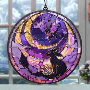 Puede incluir: Vidriera redonda con una criatura negra con alas de murciélago y un diseño de luna dorada. La obra de arte utiliza tonos de morado, dorado y negro. La vidriera está colgada de una cadena negra.
