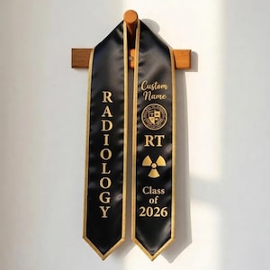 May include: Black graduation sash with gold trim and lettering. The sash reads "RADIOLOGY" vertically and includes "Custom Name," "RT," and "Class of 2026." A radiation symbol and a school emblem are also displayed.
