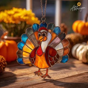 May include: A stained glass turkey ornament with a colorful fan of feathers in shades of blue, orange, yellow, and brown. The turkey has a red wattle and a small red hat. It hangs from a chain, perfect for Thanksgiving decor.