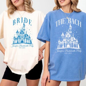 Two women wearing t-shirts with a castle design and text related to a wedding or bachelorette party.