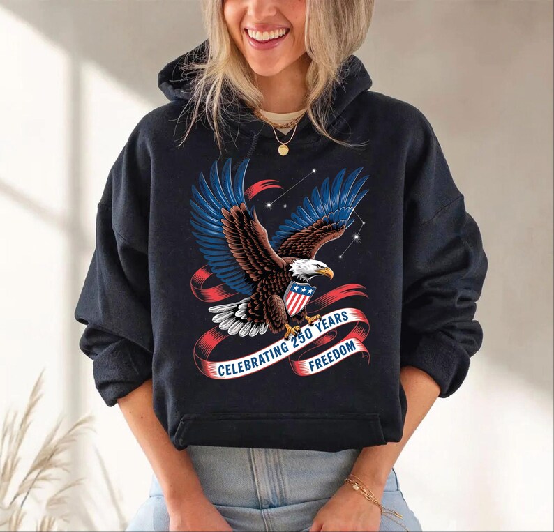 A woman wearing a black hoodie with a graphic design of an eagle and a red ribbon that says "Celebrating 250 years of freedom".