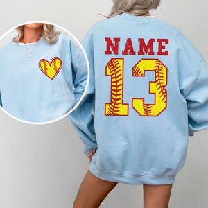 a woman wearing a light blue sweatshirt with a softball design on it