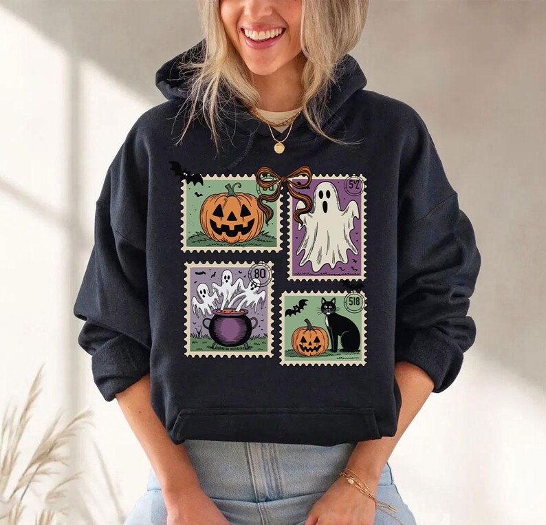 A woman wearing a black hoodie with a Halloween-themed design featuring a pumpkin, ghost, and other spooky elements.